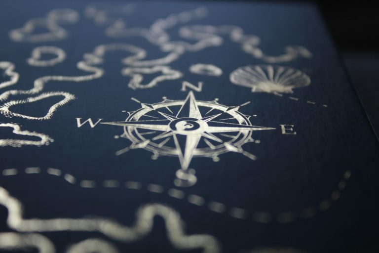 Compass and map lines in silver foil on a navy surface